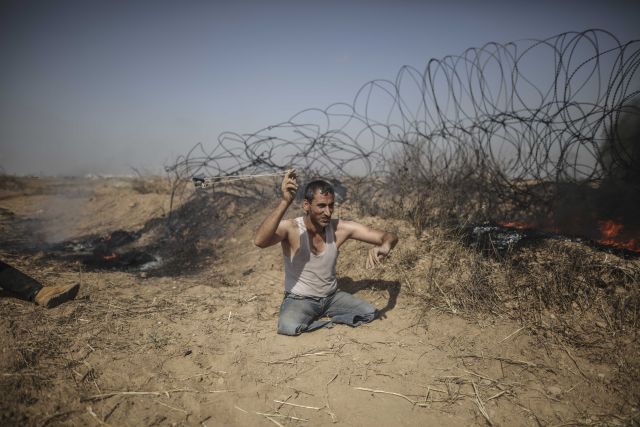 2018年5月11日A在加沙地帶東部與以色列接壤的邊境地區A一名雙腿殘疾的巴勒斯坦示威者向以色列士兵投擲石塊C新華社發(維薩姆P納薩爾攝)