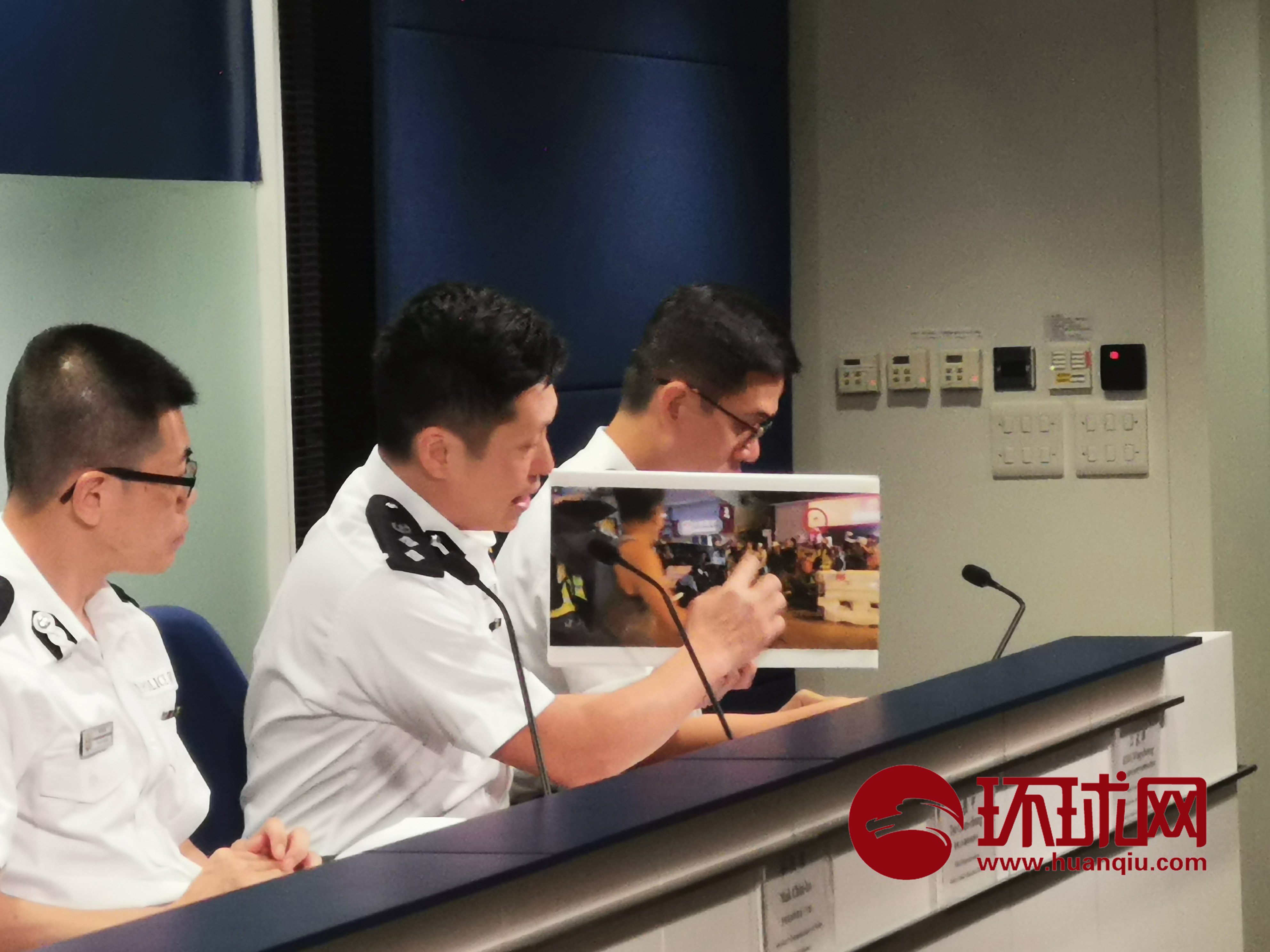 香港警隊公共關係科高級警司謝振中向媒體展示暴徒躲在一群記者身後扔磚塊雜物襲擊警方的照片，紅圈處為扔出的磚塊。（圖片來源：環球網）
