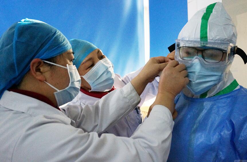 廣西壯族自治區南溪山醫院感染性疾病科醫務人員在同事的幫助下穿戴防護服。 中新社