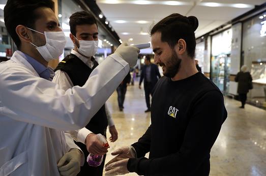 在伊朗一間商場A一男子正接受體溫檢查並進行手部消毒]美聯社資料圖^