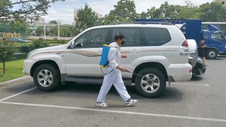 7月26日A在朝鮮平壤的大城百貨商店停車場A身着防護服的工作人員向停放車輛噴灑消毒液C]視頻截圖^